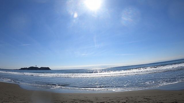 Sunny beach with calm blue water and a distant small island on the horizon.