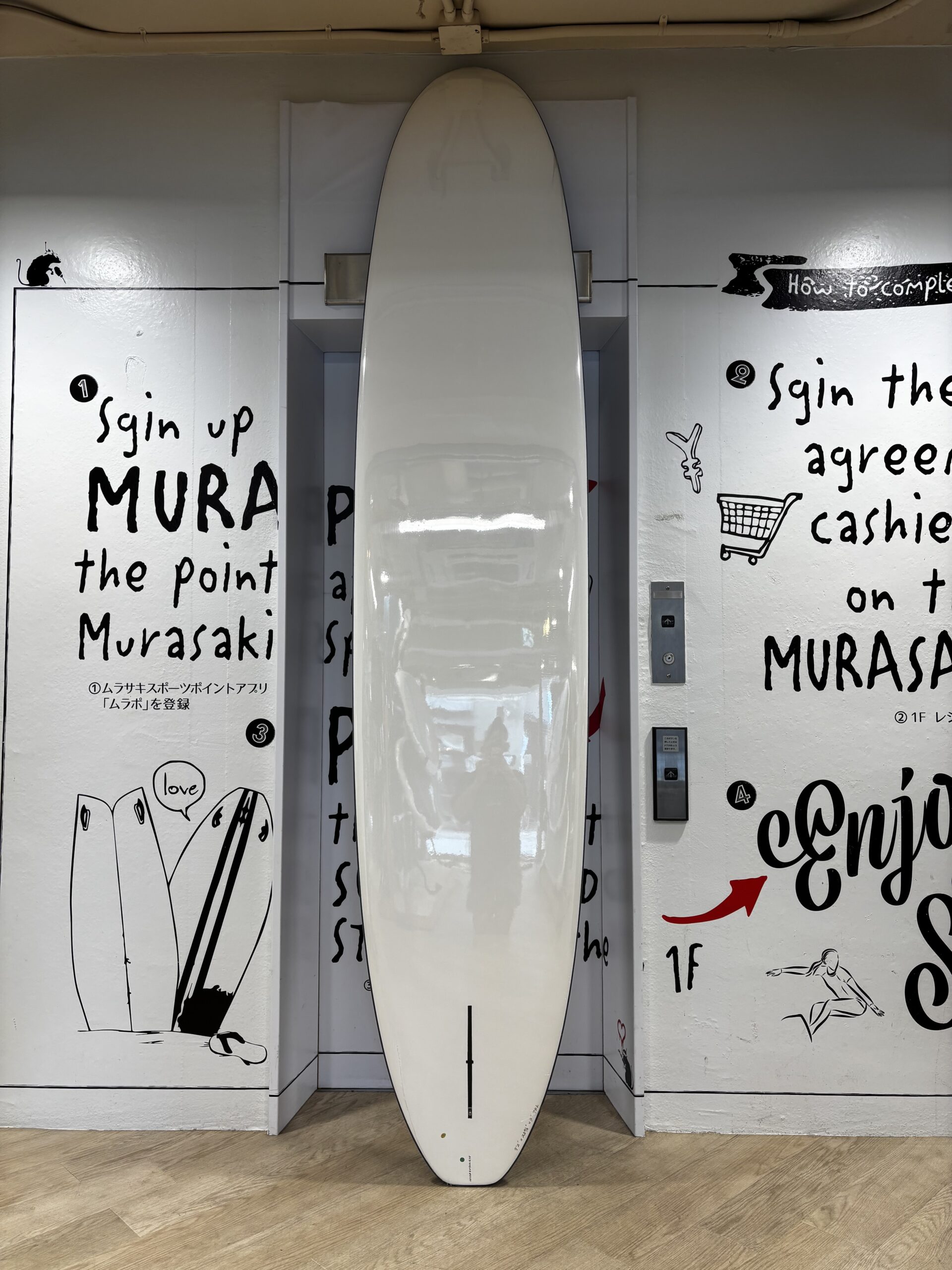 IMG_1129 - SHOP NEWS | ムラサキスポーツオンラインストア 通販 White surfboard standing upright in a wall alcove, surrounded by black handwritten text and drawings on the walls.