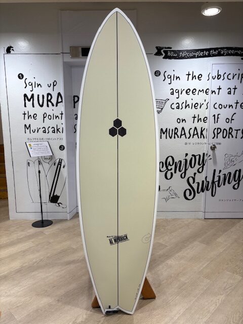 Beige surfboard on a wooden stand indoors, centered against a wall with black text and drawings, white rail edges and a small logo near the middle