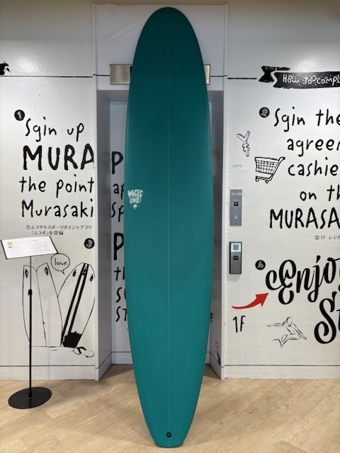 IMG_8836 - SHOP NEWS | ムラサキスポーツオンラインストア 通販 Teal surfboard standing upright between two doors with white walls covered in black graffiti and drawings on either side.