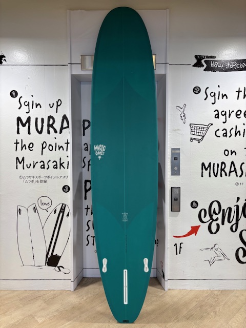 IMG_8841 - SHOP NEWS | ムラサキスポーツオンラインストア 通販 Teal surfboard standing upright in a doorway between graffiti-covered white walls indoors.