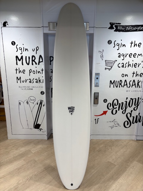 IMG_8847 - SHOP NEWS | ムラサキスポーツオンラインストア 通販 White surfboard standing upright on a wooden floor between graffiti-covered walls in a shop.
