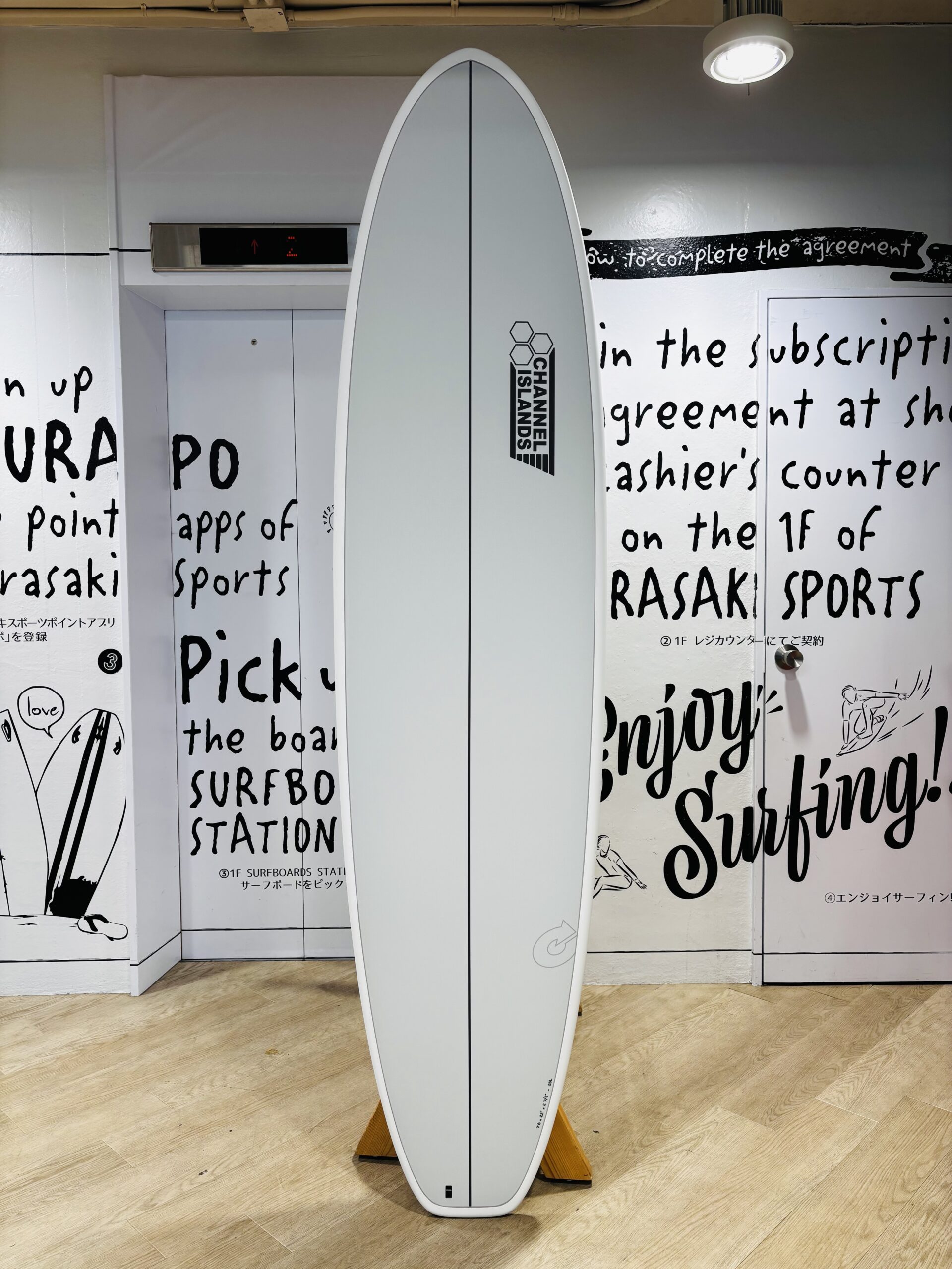 IMG_9968 - SHOP NEWS | ムラサキスポーツオンラインストア 通販 White surfboard standing upright on a wooden floor indoors, with a vertical center seam and Channel Islands logo down the middle.