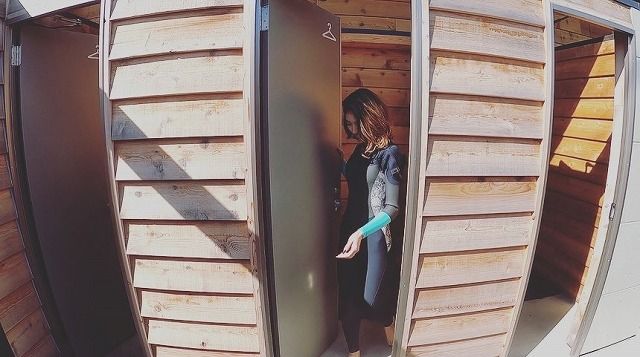 Woman in a denim jacket opens a tall door between wooden storage lockers or sheds.