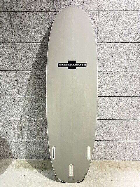 s-IMG_7410 - SHOP NEWS | ムラサキスポーツオンラインストア 通販 Tall pale gray surfboard leaning against a concrete block wall, featuring a 'Water Rampage' logo and three fin boxes at the bottom wall side edge.
