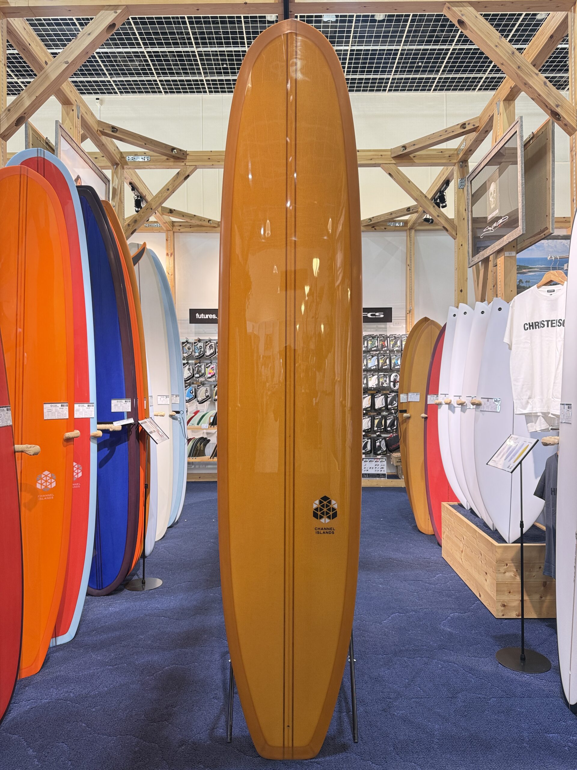 Tall orange surfboard upright in a shop aisle, with colorful boards lined along both sides.