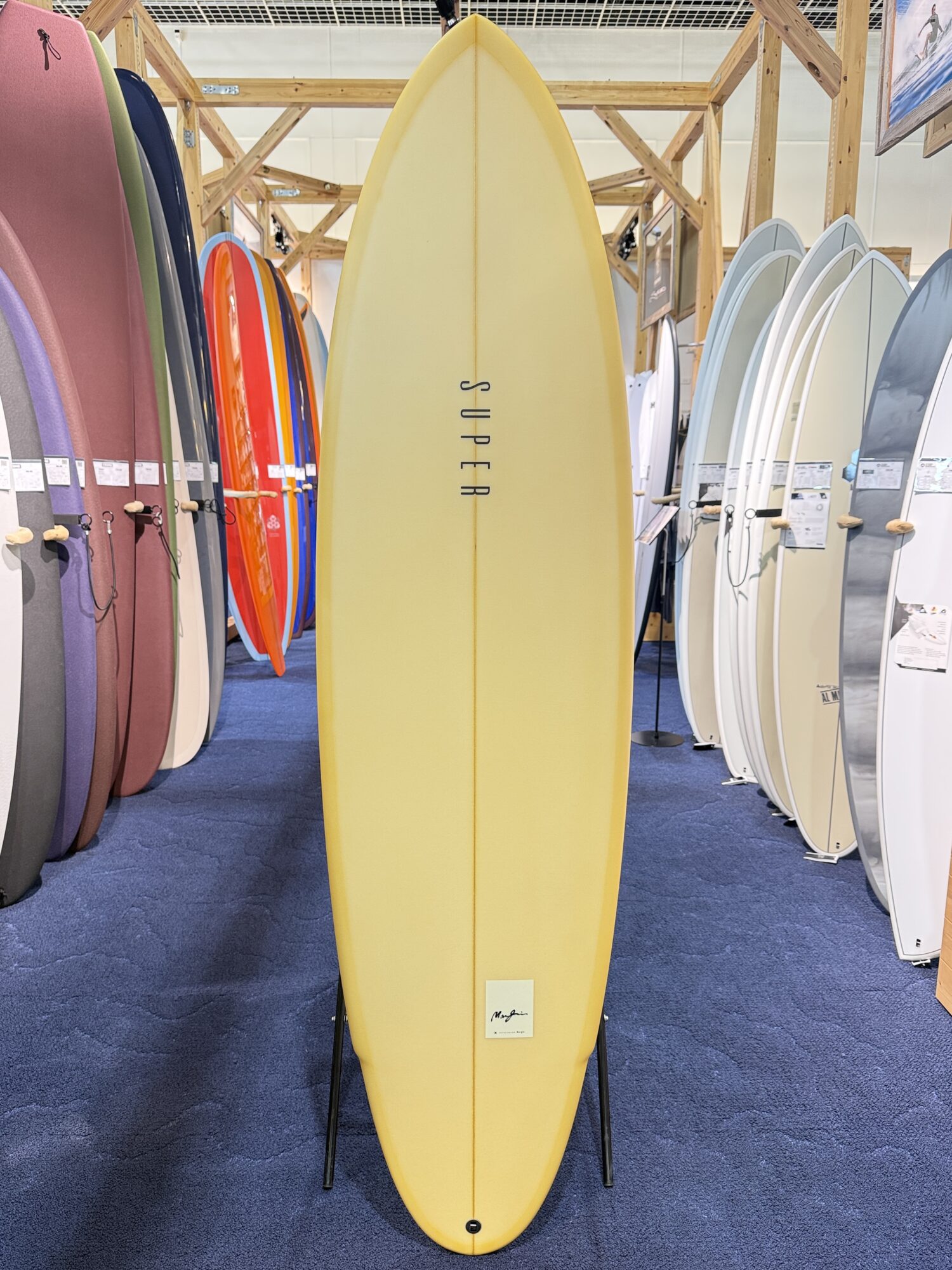 Yellow longboard surfboard on a display stand in a showroom, surrounded by colorful boards on racks.