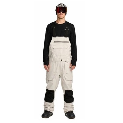 Person wearing beige snow bib overalls with knee pads, black long-sleeve shirt, goggles, and helmet.