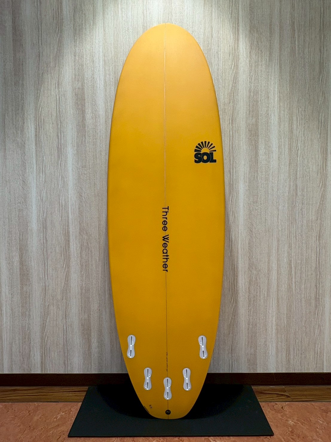 Bright yellow surfboard standing upright with six tail fins, SOL logo, and 'Three Weather' text down the center.