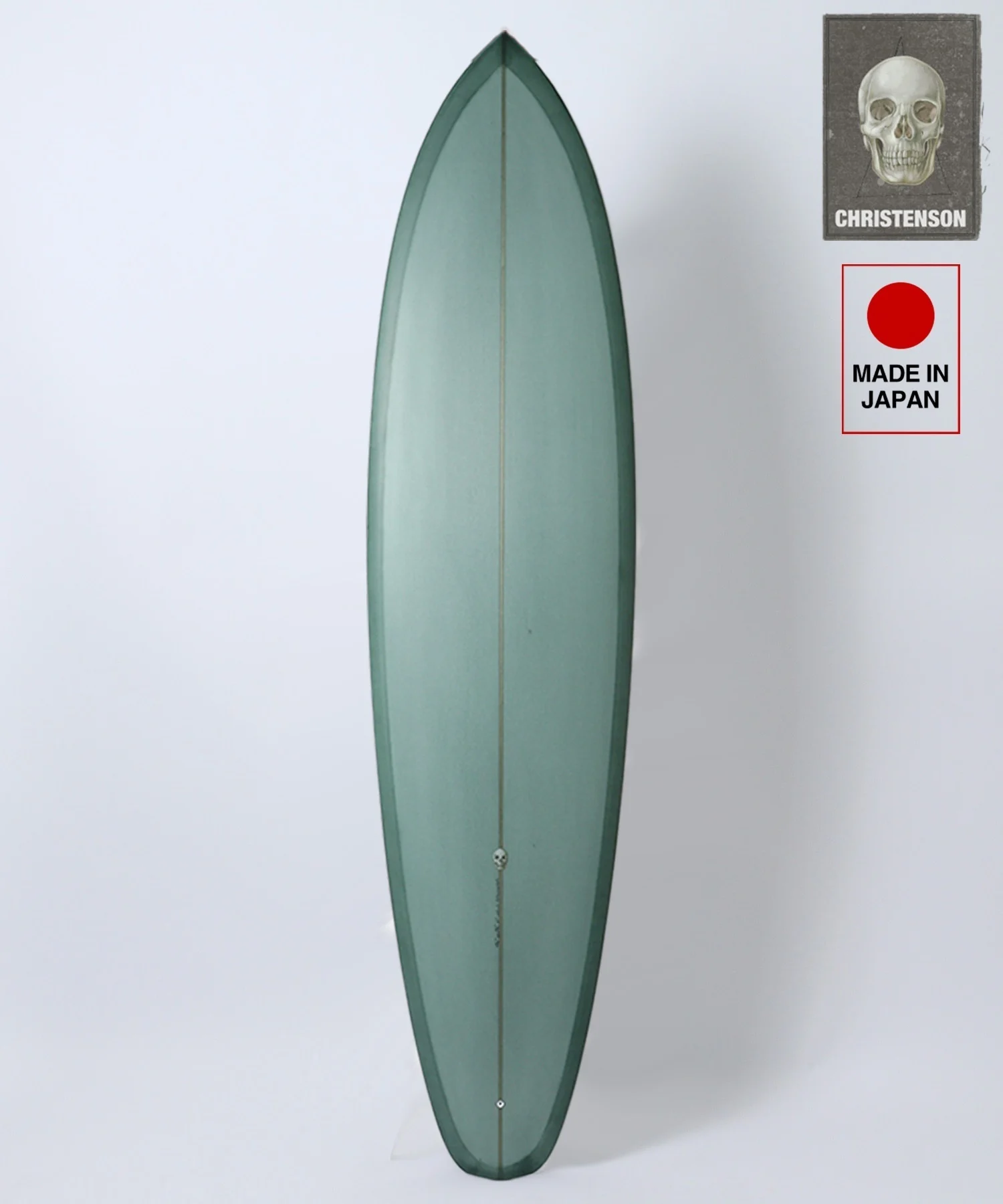 image - SHOP NEWS | ムラサキスポーツオンラインストア 通販 Teal surfboard standing upright against a white backdrop, with two labels on the upper right: a skull image and 'Made in Japan' text.
