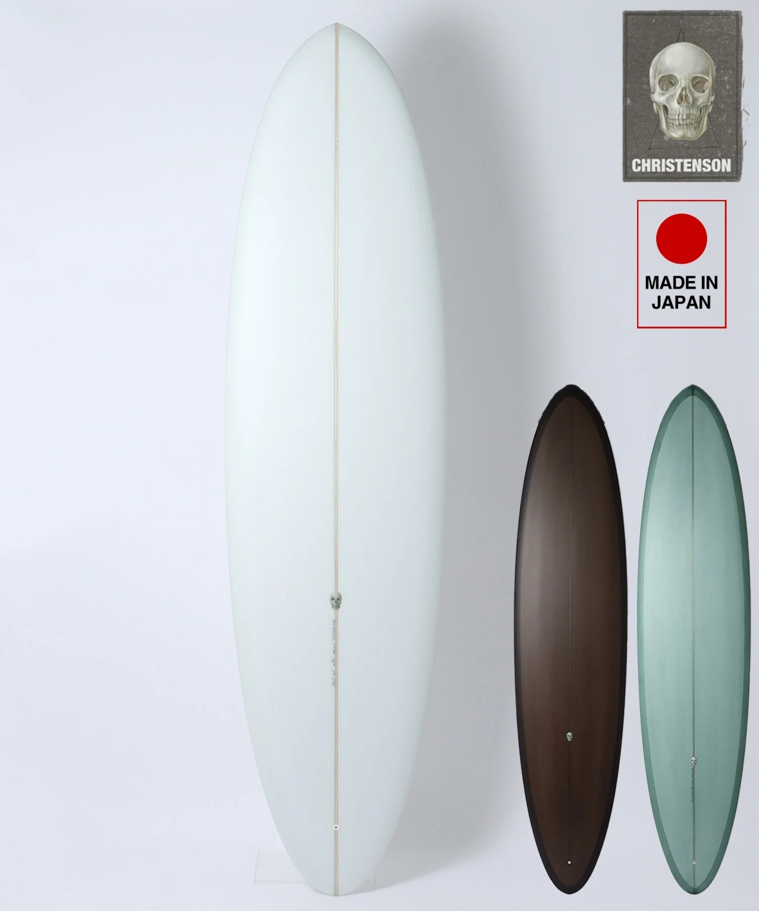image - SHOP NEWS | ムラサキスポーツオンラインストア 通販 Tall pale blue surfboard standing upright against a white wall with three smaller brown, green, and black boards beside it; brand tag visible on top right.