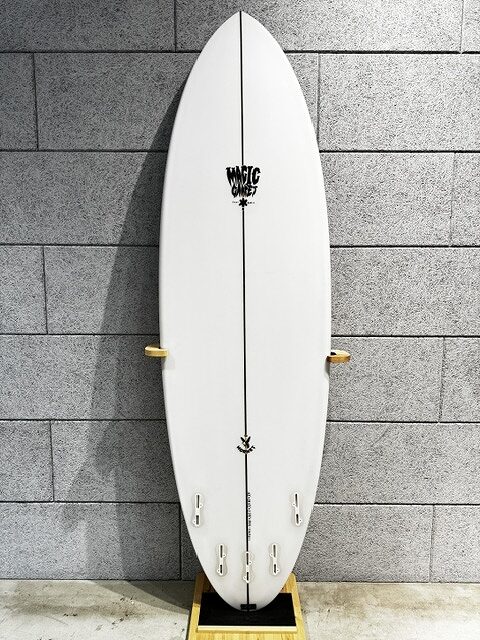 s-IMG_4250 - SHOP NEWS | ムラサキスポーツオンラインストア 通販 White surfboard standing upright on a wooden stand against a gray brick wall.