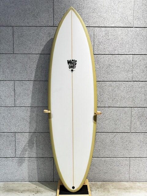 s-IMG_4253 - SHOP NEWS | ムラサキスポーツオンラインストア 通販 White surfboard with yellow rails stands upright on a wooden rack against a gray brick wall.