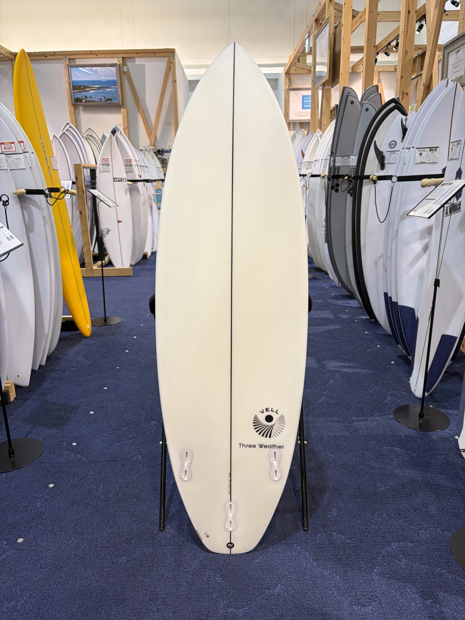 White surfboard standing upright in a crowded showroom with many boards on display around it.