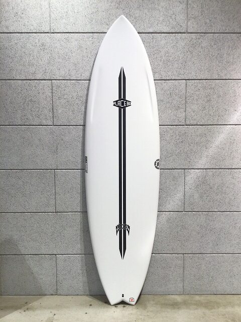 White surfboard with a black double stripe and small logos, standing upright against a gray tiled wall.
