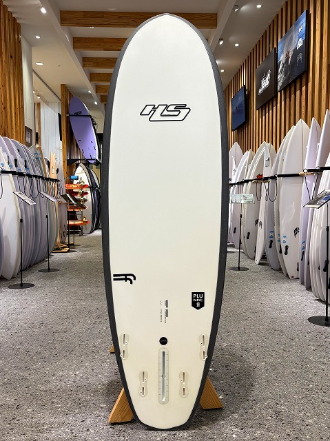White surfboard with a black edge on a display rack in a surf shop, surrounded by many other boards on both sides.