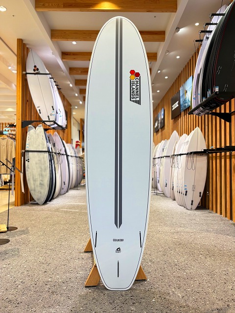 a-image1 - SHOP NEWS | ムラサキスポーツオンラインストア 通販 White surfboard on a stand in a surf shop, featuring a vertical gray center stripe and Channel Islands logo near the top.