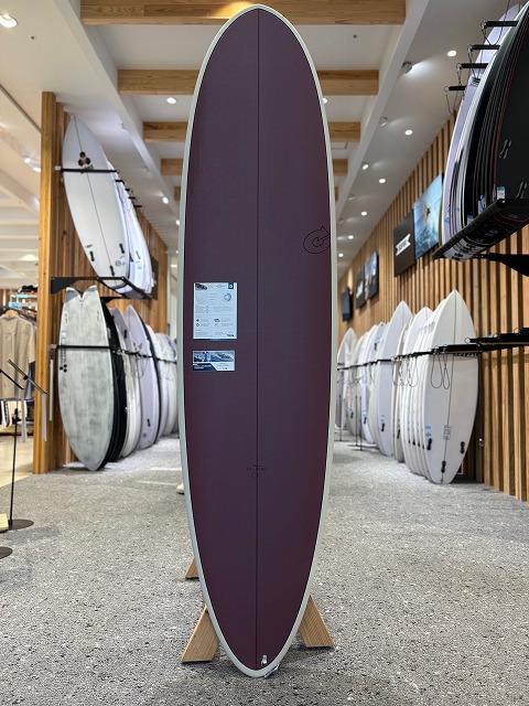 b-image7 - SHOP NEWS | ムラサキスポーツオンラインストア 通販 Purple surfboard on a display stand in a showroom, with racks of white boards along both walls.