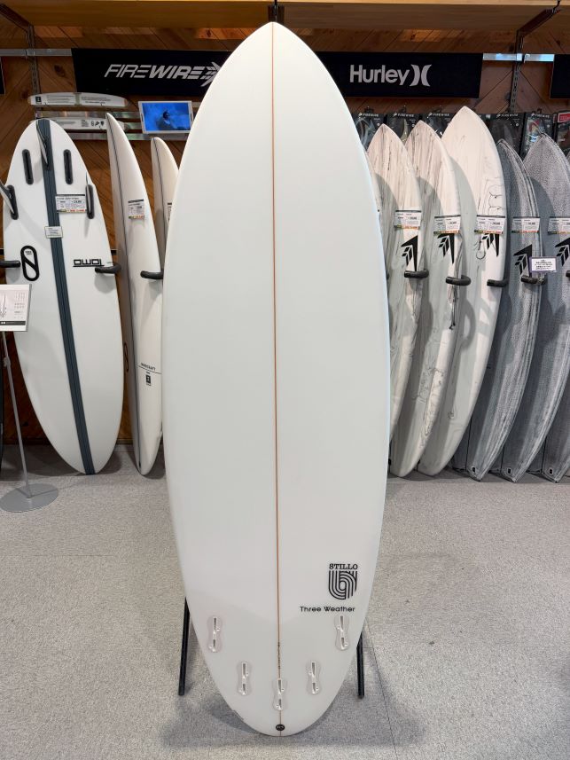 White surfboard on a stand in a surf shop, with other boards displayed behind it.
