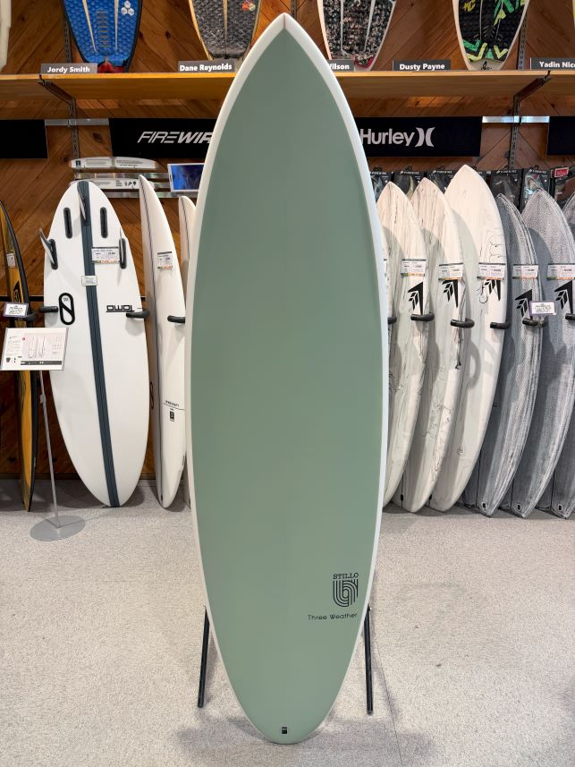 Mint green surfboard on a display rack in a shop, with white and gray boards lined up behind it.