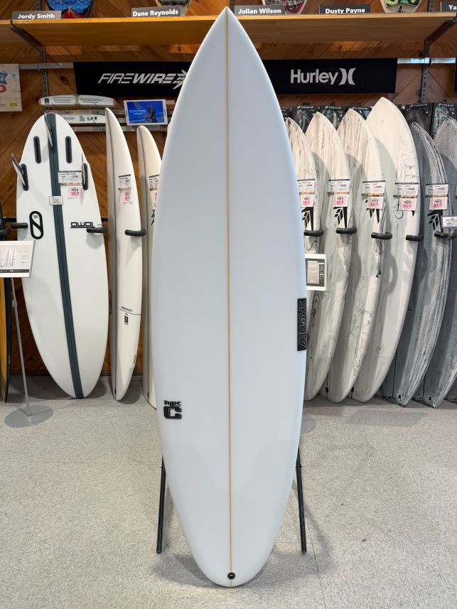 White surfboard on a display stand in a surf shop, with other boards in the background.