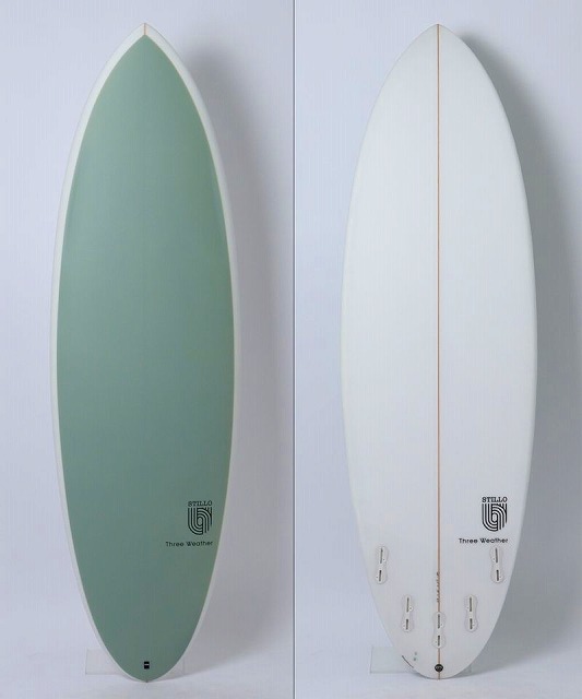 Two surfboards standing upright side by side against a pale wall: left green board with white border, right white board with an orange stringer and multiple fins on the bottom edge.