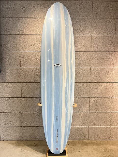 Blue-and-white striped surfboard standing upright against a beige brick wall on a wooden rack, ready for display or storage.