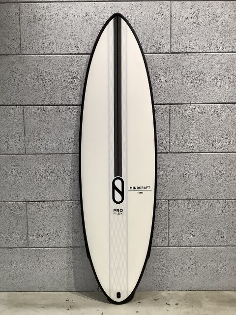 s-IMG_6436 - SHOP NEWS | ムラサキスポーツオンラインストア 通販 White surfboard with a black center stripe, pro model, leaning against a gray brick wall; Mindcraft Tokyo branding visible.