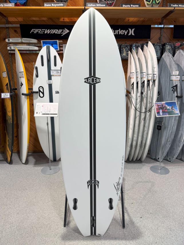 White surfboard with a double black center stripe and Placebo logo, standing on a display rack in a shop.