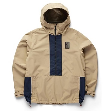 LS1 SHELL ANORAK - SHOP NEWS | ムラサキスポーツオンラインストア 通販 Beige hooded windbreaker with a dark blue center panel, navy side pockets, and a chest logo patch.