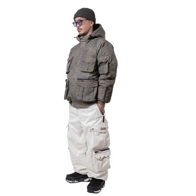 Man in a gray insulated parka, black beanie, sunglasses, and beige cargo pants, standing with hands in pockets.