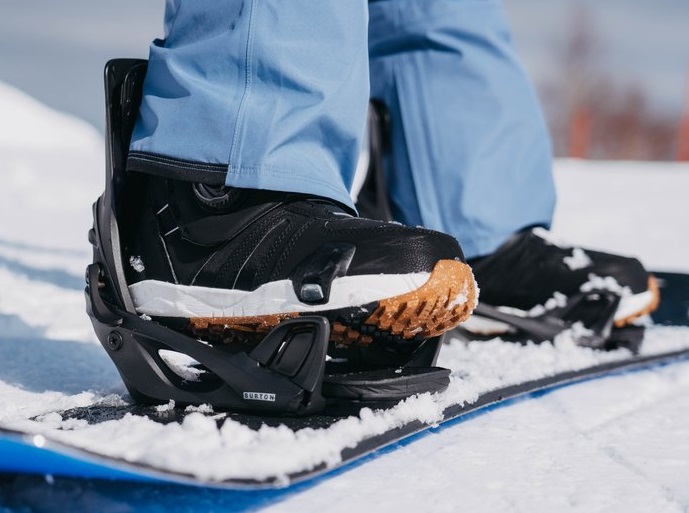 Close-up of a black snowboard boot clipped into a binding on a snow-covered board