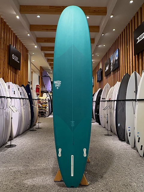 a-image1 - SHOP NEWS | ムラサキスポーツオンラインストア 通販 Teal surfboard on a display rack in a surf shop, surrounded by other boards on both sides.