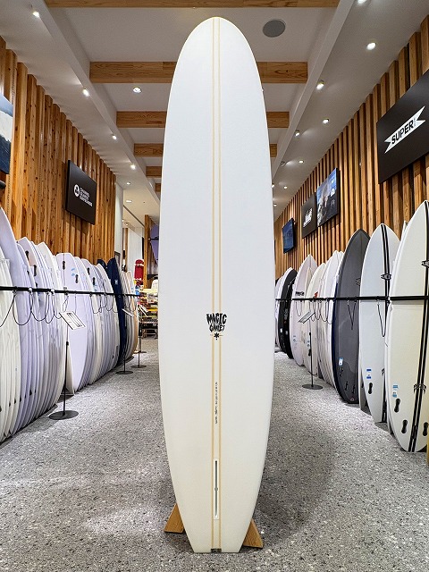 a-image3 - SHOP NEWS | ムラサキスポーツオンラインストア 通販 Central white surfboard on display in a shop, indoors with wooden walls and other boards lined up on both sides.