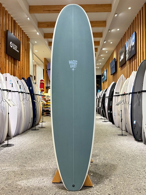 a-image8 - SHOP NEWS | ムラサキスポーツオンラインストア 通販 Teal surfboard on a wooden stand in a showroom, surrounded by other boards on racks.