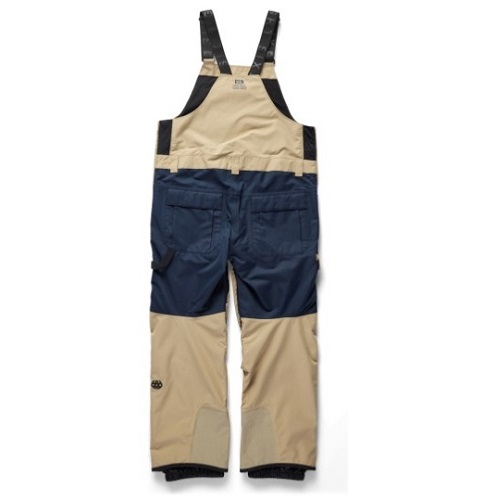 Back view of two-tone beige and navy bib pants with black suspenders, showing rear pockets and color-blocked panels.