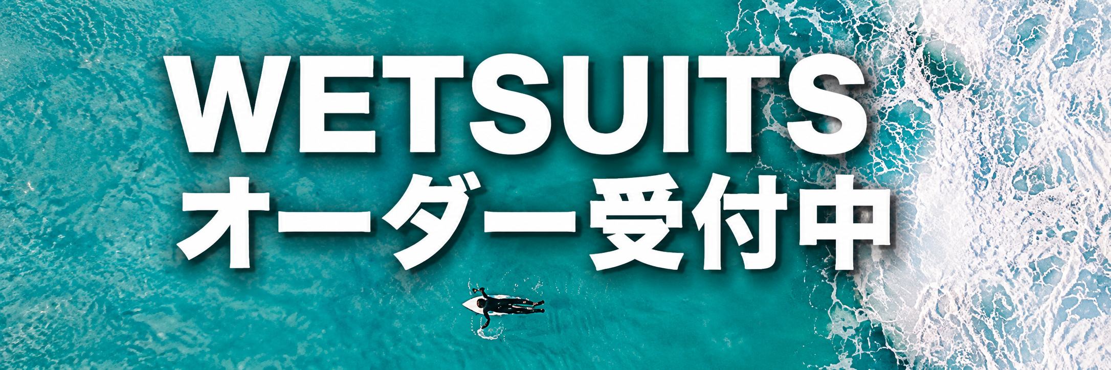 Bold white text 'WETSUITS' and Japanese characters on a turquoise ocean background with a surfer in the water.