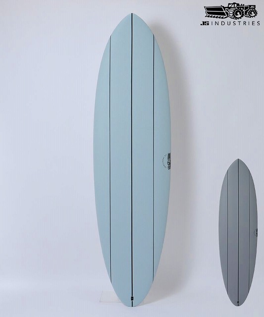 BIG BARON SOFT 1 - SHOP NEWS | ムラサキスポーツオンラインストア 通販 Tall light-blue surfboard displayed upright on a stand, with a smaller gray board next to it on a white wall (JS Industries logo in corner).