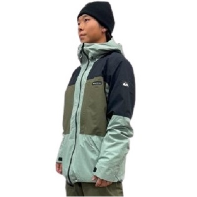 Person wearing a color-blocked outdoor jacket in light green, olive, and navy, with a black beanie.
