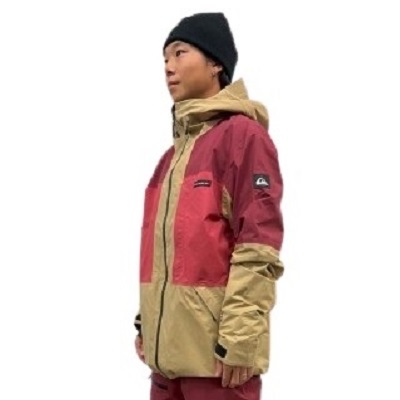 Person in a red and tan color-blocked outdoor jacket with a black beanie, viewed in profile.