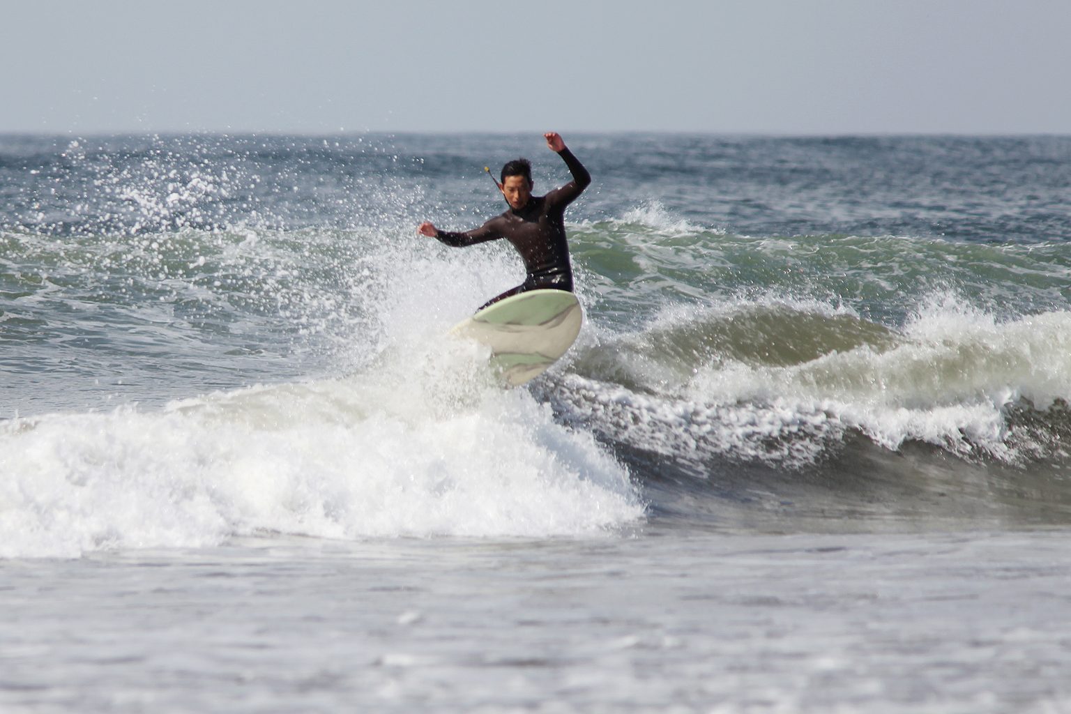 Hires_HI__RU_IMG_4888-1536x1024 - SHOP NEWS | ムラサキスポーツオンラインストア 通販 Surfer in a black wetsuit rides a breaking wave with a white-green board, spray flying around the surfer.