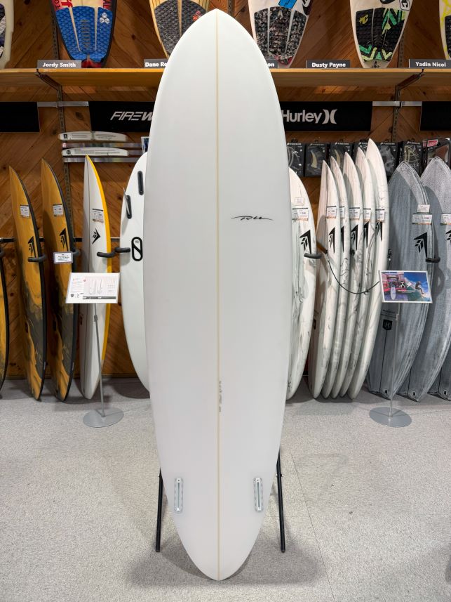IMG_9513 - SHOP NEWS | ムラサキスポーツオンラインストア 通販 White surfboard on a stand in a surf shop, with other boards on racks in the background.