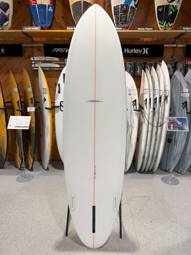 IMG_9526 - SHOP NEWS | ムラサキスポーツオンラインストア 通販 White surfboard on a display stand in a shop, centered with other boards on racks behind.