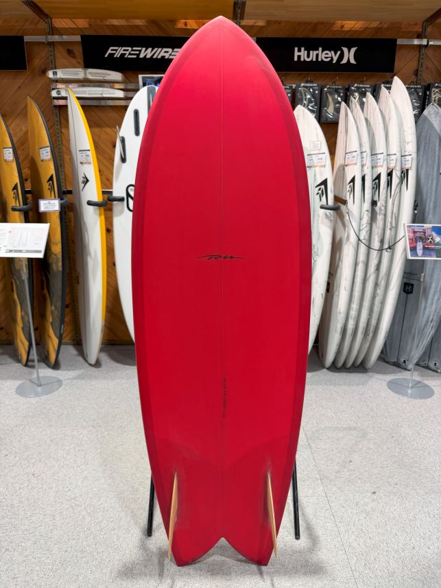 IMG_9538 - SHOP NEWS | ムラサキスポーツオンラインストア 通販 Red surfboard on display in a surf shop with other boards visible in the background.