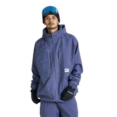 Man wearing a blue zip-up winter jacket with large front pockets, black gloves, a blue beanie, and ski goggles on his head.