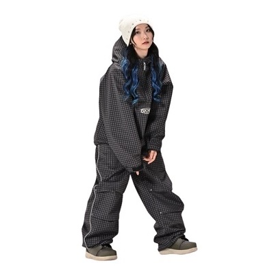Woman wearing a loose black dotted snowsuit with a cream knit beanie, blue hair visible, standing with hands together against a white background.