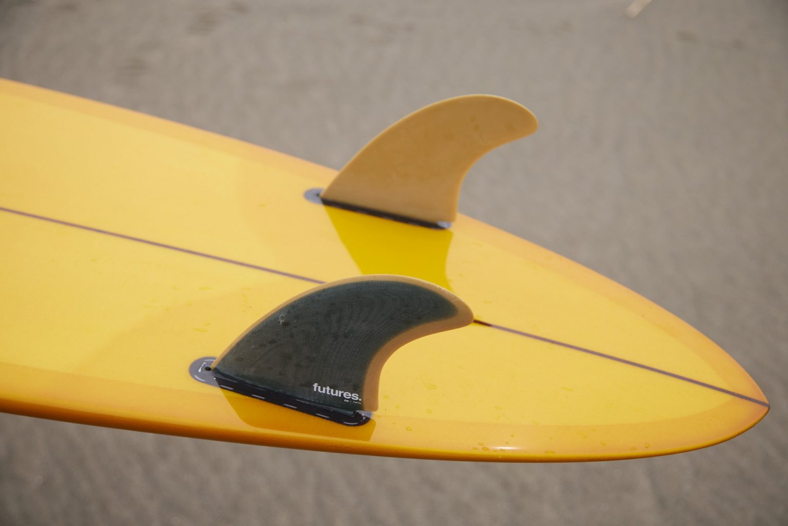 YU-SURF-CLASSIC-Arcana_3-1536x1025 - SHOP NEWS | ムラサキスポーツオンラインストア 通販 Close-up of a yellow surfboard tail with two fins: a black Futures fin and a smaller beige fin