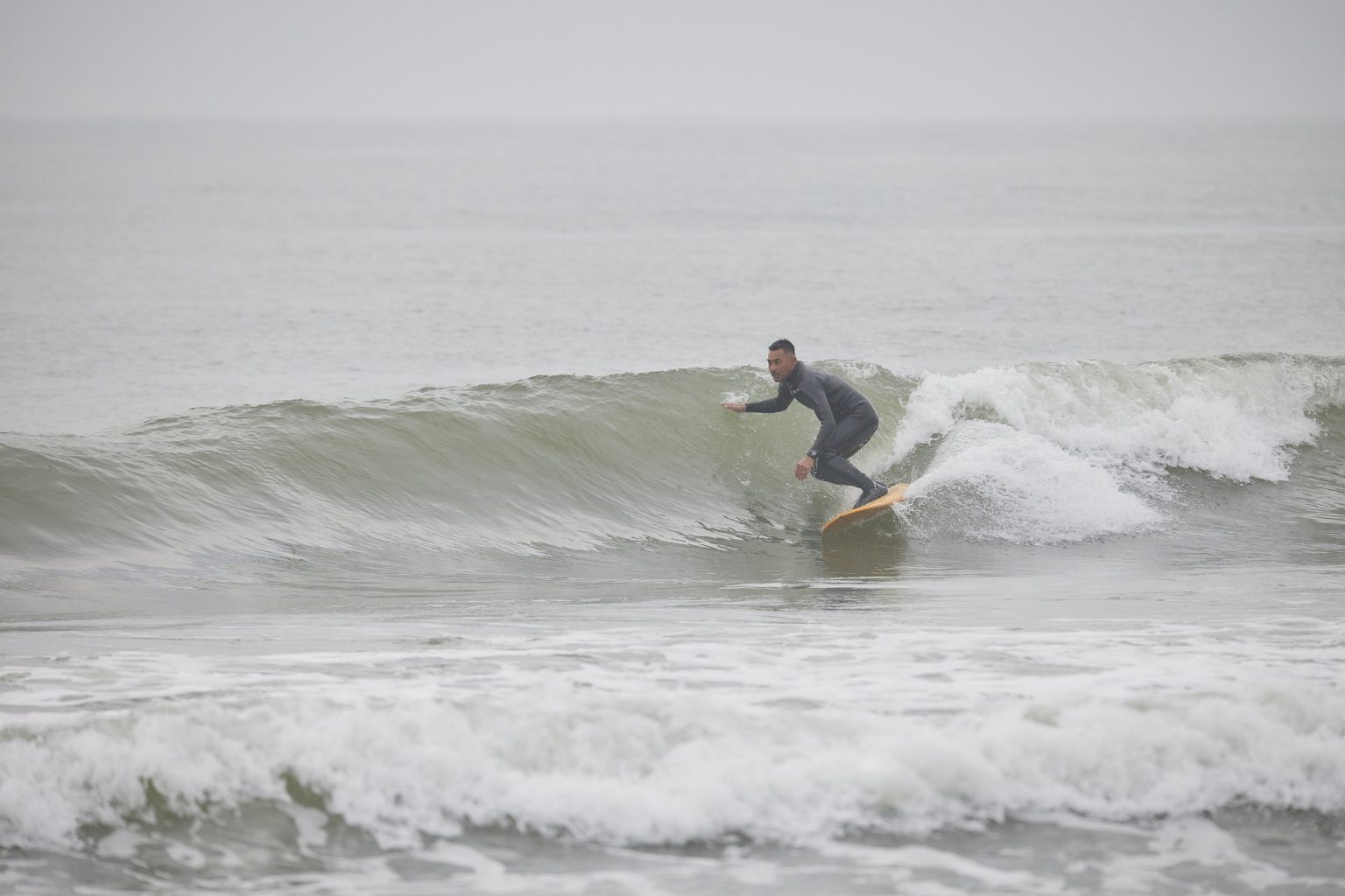 YU-SURF-CLASSIC-Arcana_4-1536x1024 - SHOP NEWS | ムラサキスポーツオンラインストア 通販 Surfer in a black wetsuit rides a green-tinted wave on a yellow board.