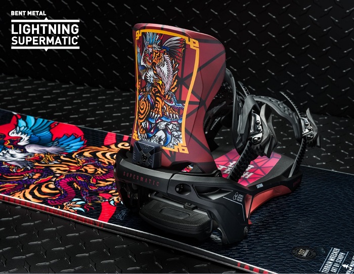 Snowboard binding with a bold red and black design mounted on a graphic snowboard, branding reads Lightning Supermatic/ Bent Metal at the top left.