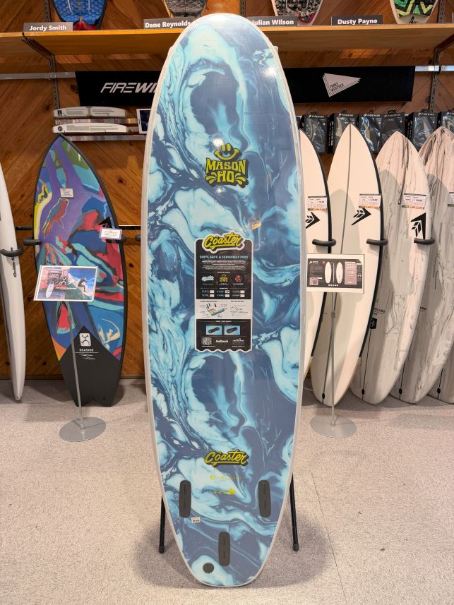 Blue marbled surfboard on a display rack in a shop, with Mason Ho Coaster branding and a product label near the center.